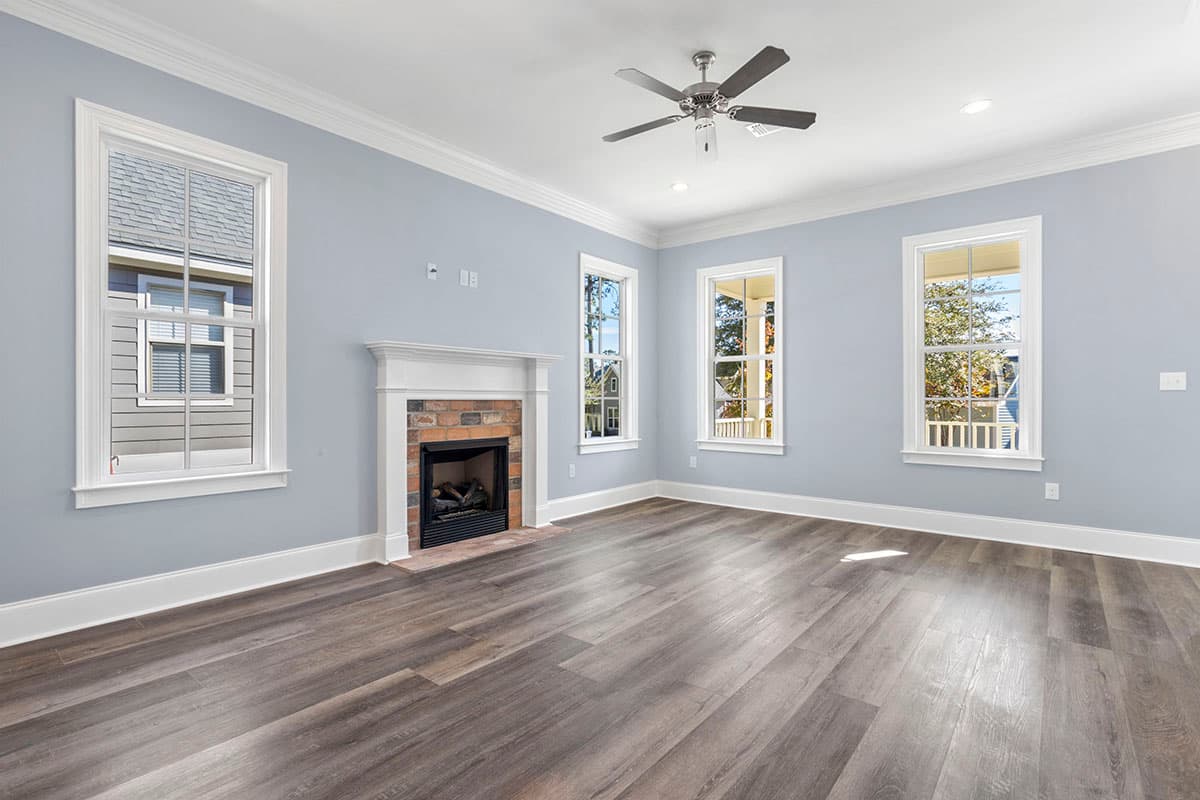 Interior view of a room with a brick fireplace, ceiling fan, multiple windows, and wood-look flooring.
