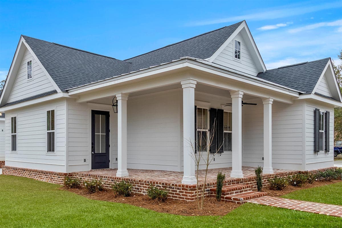 House plan exterior: White sided cottage with covered porch, brick accents, gables, and dormer.