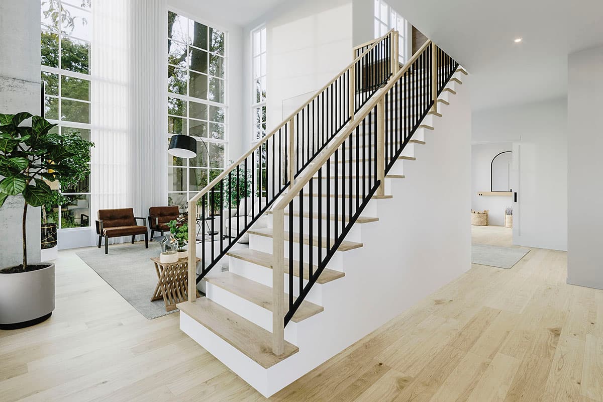 Interior view of a house showing a modern staircase with wooden treads and black balusters, and tall windows in the background.