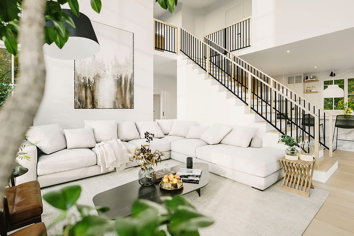 Interior rendering of a great room with a sectional sofa, open staircase, and view into the kitchen.