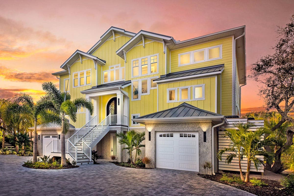 House plan exterior. Two-story home with a hipped roof, dormers, and a prominent entryway with stairs. Attached garage on the right.