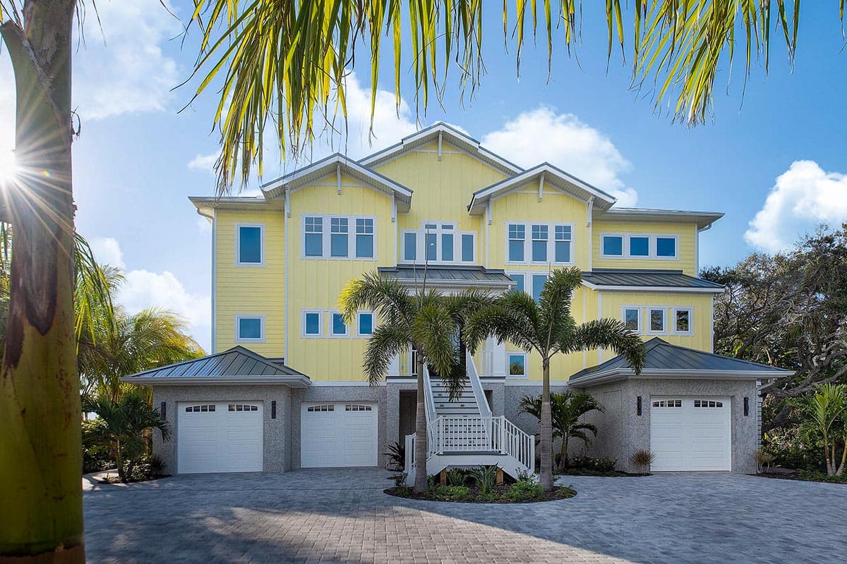 House plan exterior: Yellow, three-story coastal home with multiple gables, standing seam roof, and three-car garage.
