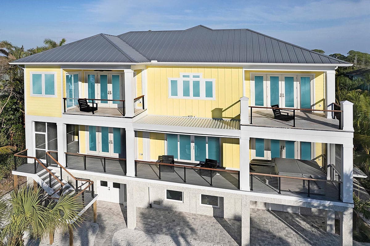 House plan exterior: Three-story residence with metal roof, multiple balconies, glass doors, and covered lower level.