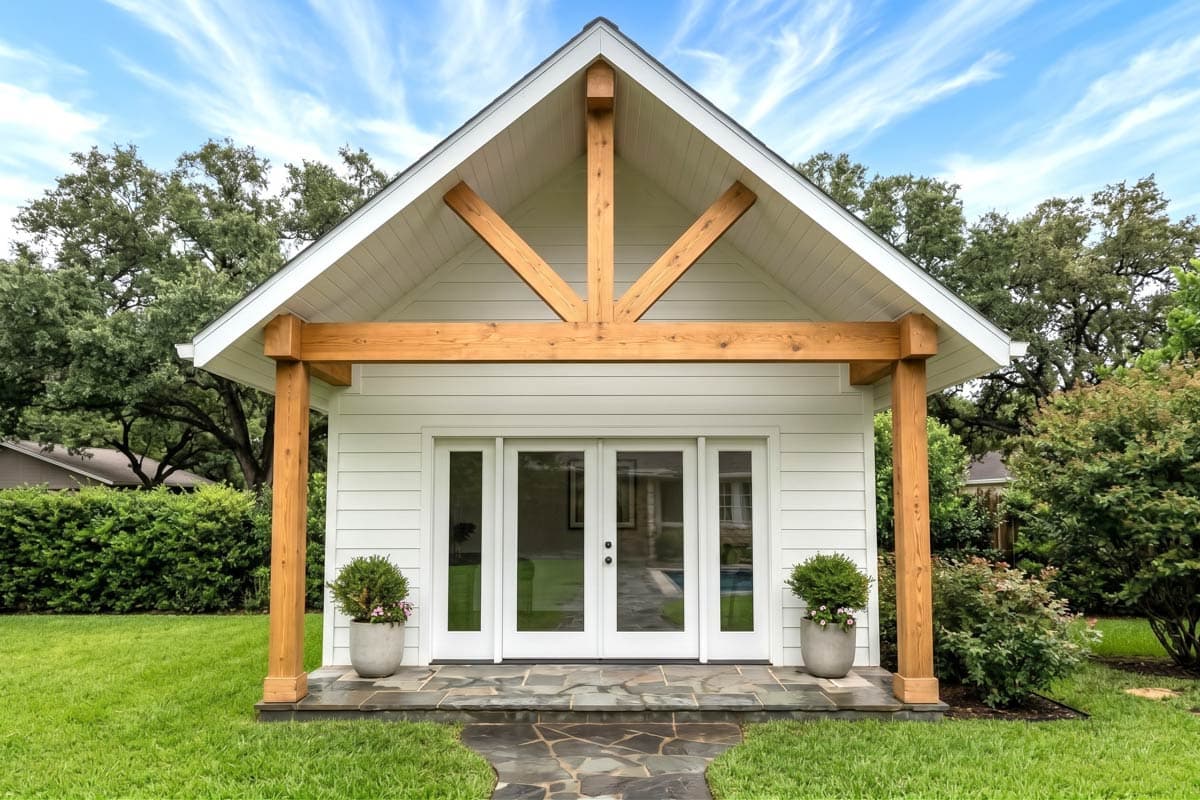 House plan exterior. One-story structure with gabled roof, exposed rafters, and covered porch area. Features a pool and outdoor seating area.