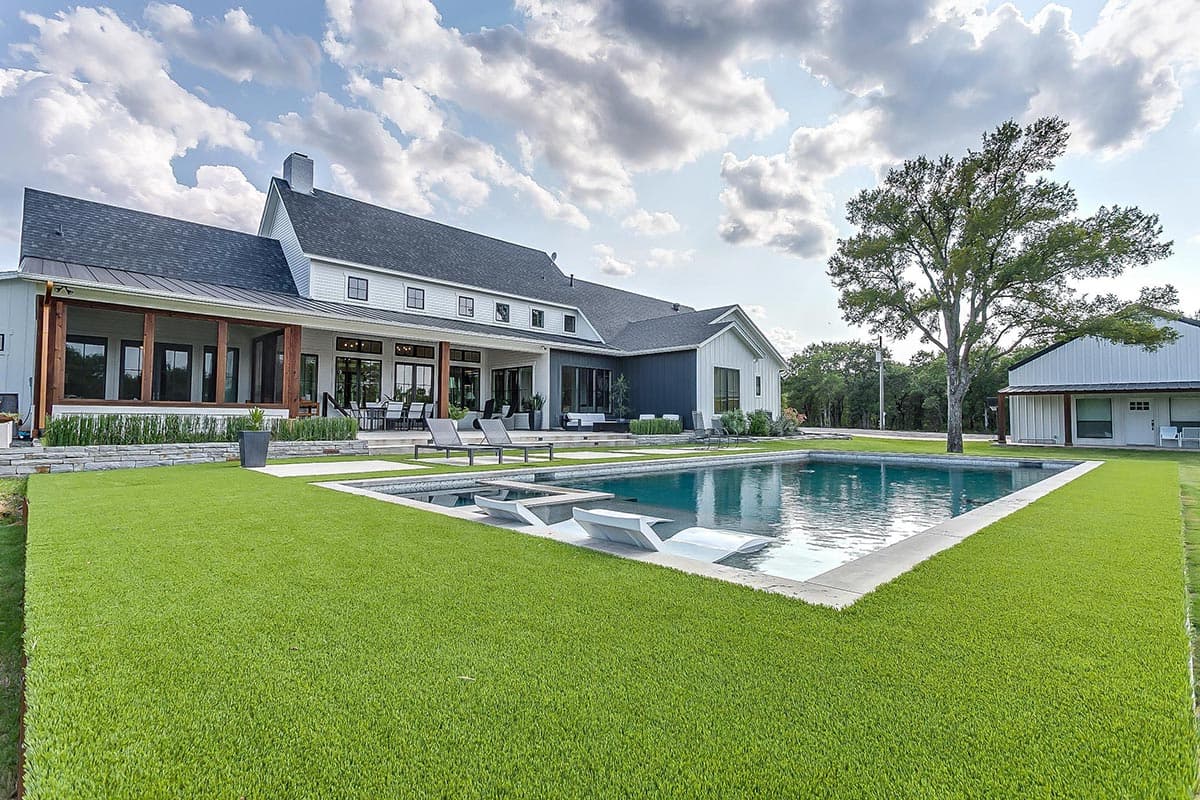 Modern farmhouse exterior with pool, wraparound porch, multiple gables, and dark metal roof.