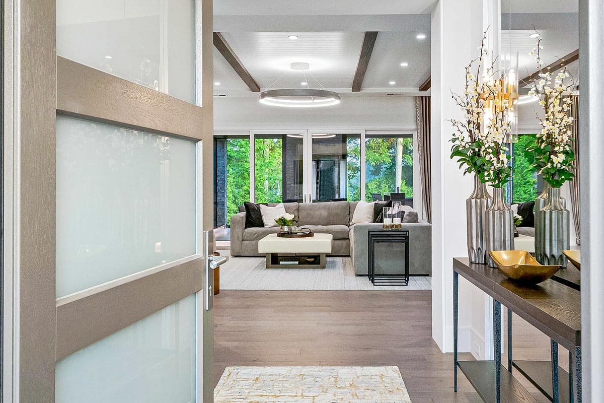 Interior view of a great room with a sectional sofa, modern circular chandelier, and large windows overlooking greenery.