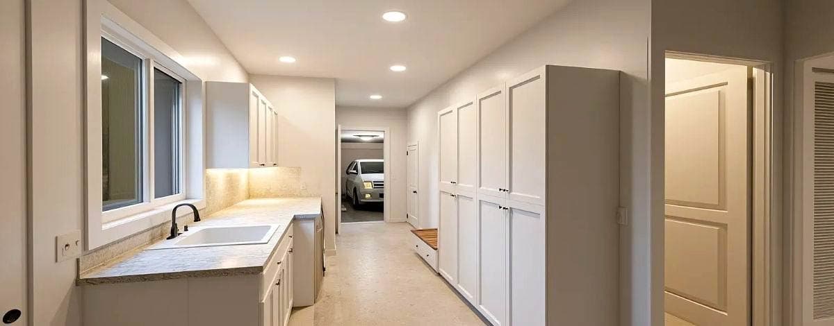 Bright, modern entryway with a utility sink, large cabinets, and a view of a car parked in the garage. Natural light floods the space.