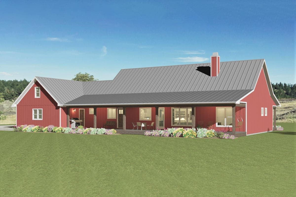 A red farmhouse with a gray roof and a covered porch. The home sits on a large green lawn, with colorful flowers lining the front.