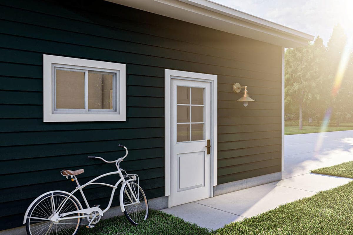 House plan exterior with dark siding, white paneled door with glass panes, and a sliding window. A bicycle rests nearby.