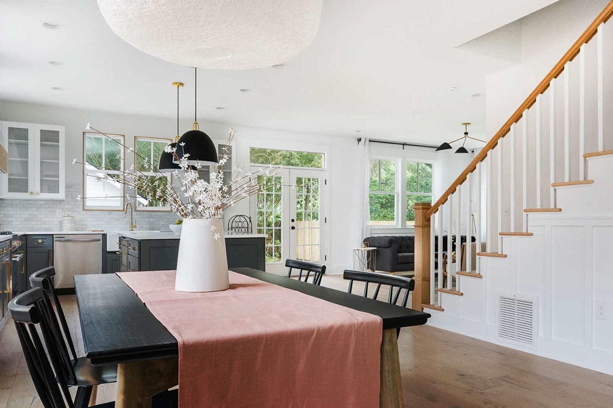Open-concept dining and kitchen area with island, staircase with wooden railing, and glass-paneled doors leading outside.