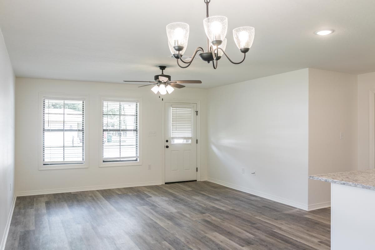 Interior view of an open-concept living area with wood-look flooring, two windows, a door, and ceiling fans.