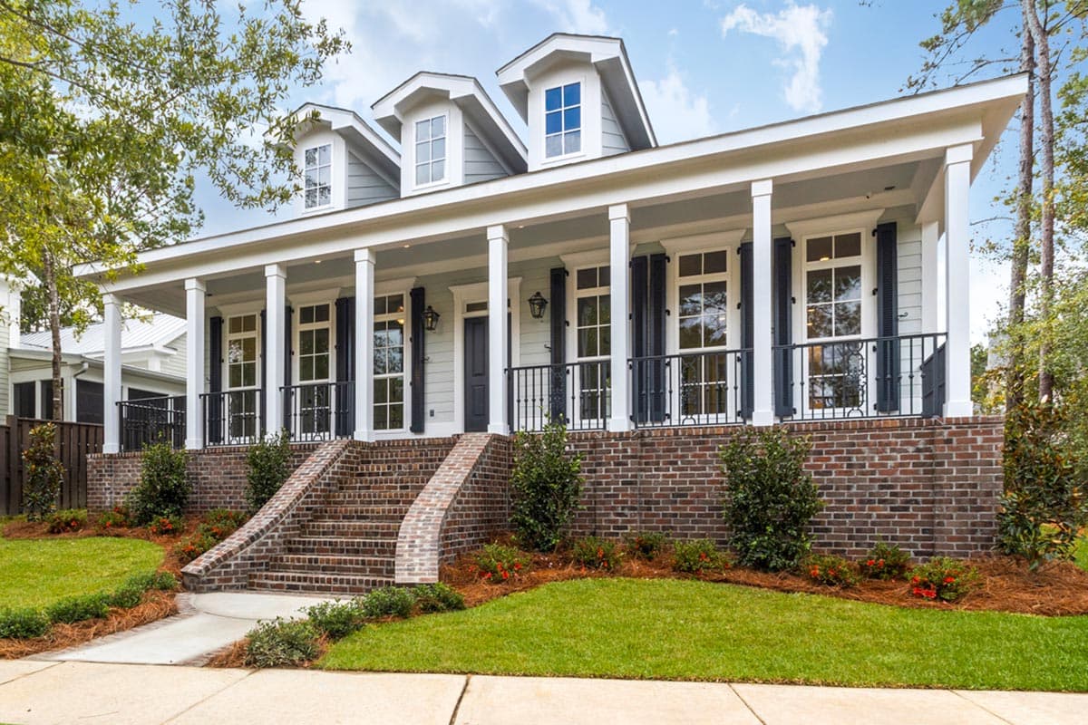 House plan exterior with two stories, a wide front porch with columns, dormers, and brickwork on the foundation.