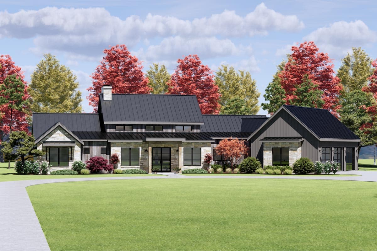A modern, ranch-style home with a black metal roof, stone accents, and a long driveway. Autumn trees frame the house against a cloudy sky.