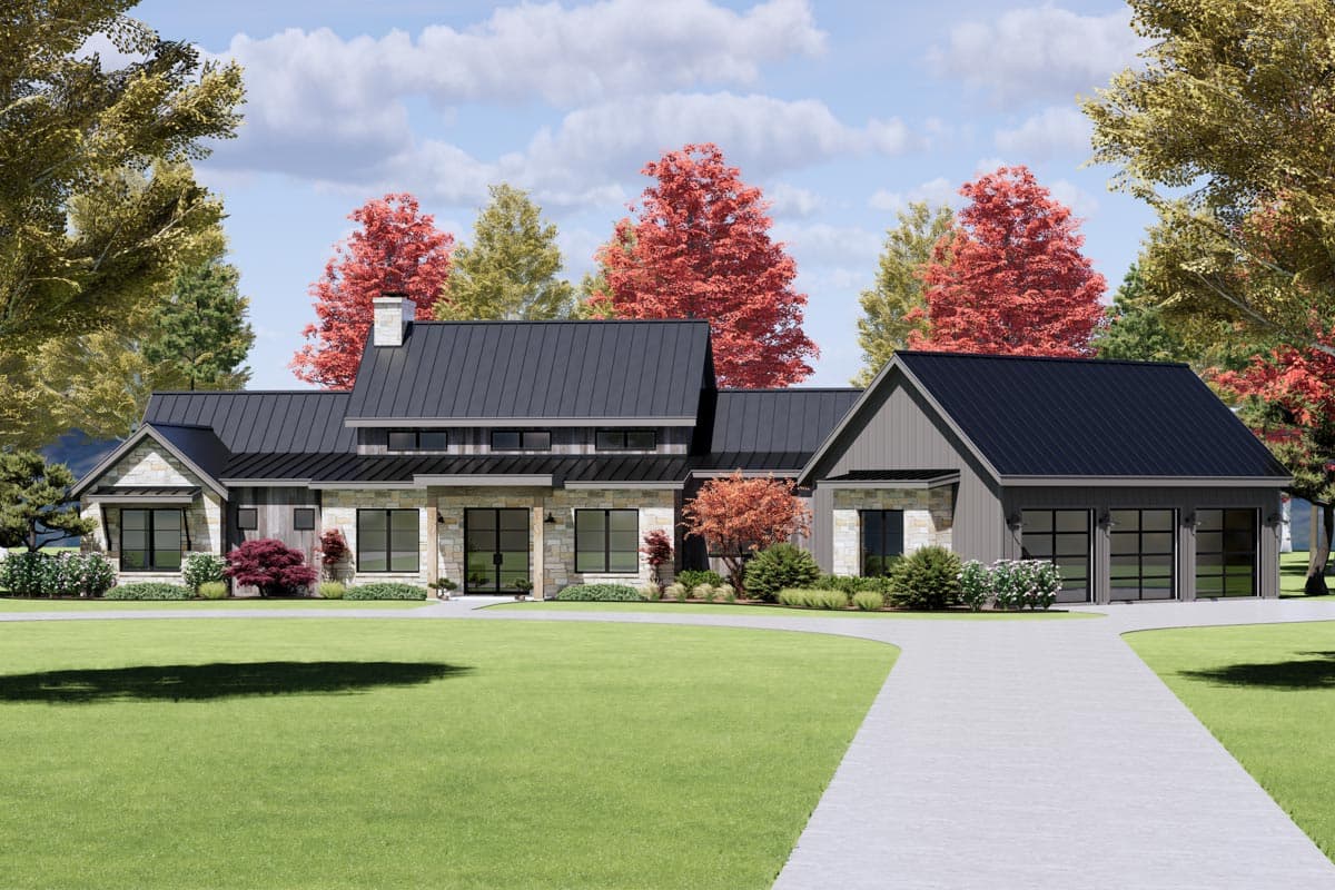 A modern, single-story house with a dark gray roof, stone accents, and a long driveway. Trees with colorful fall foliage surround the home.
