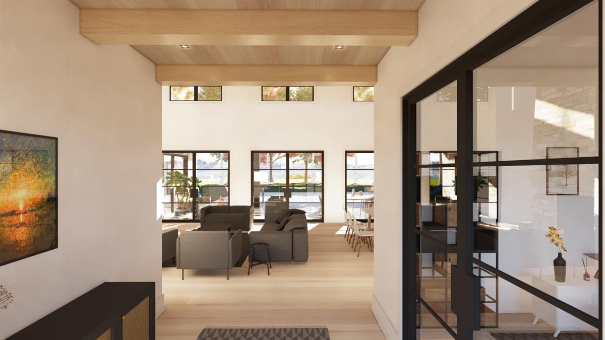 An open, modern home interior features wooden beams, large windows, and a view into a living space with grey couches, and a dining area.