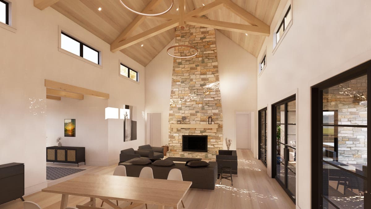 Spacious living room with vaulted ceiling, stone fireplace, and large windows. Furnished with a sofa, dining table, and modern decor in a bright interior.