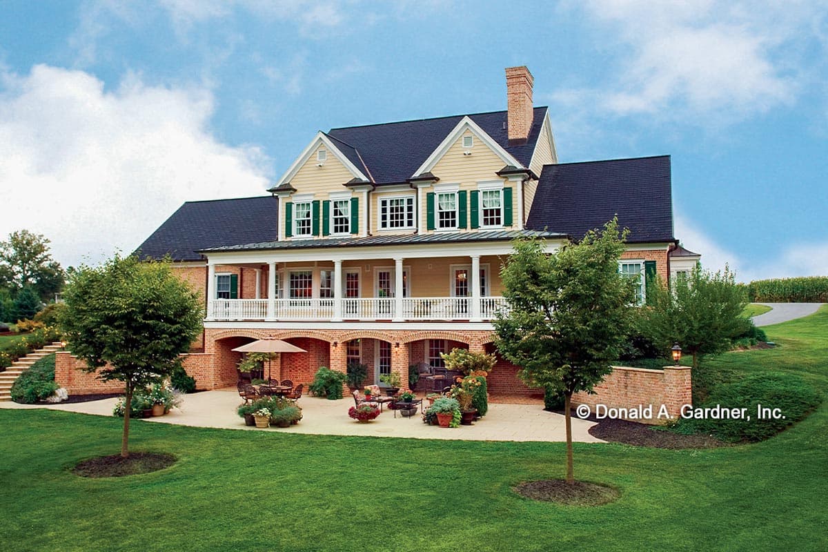 House plan exterior, two-story, with wrap-around second-story porch, arched brick base, and multiple gables.