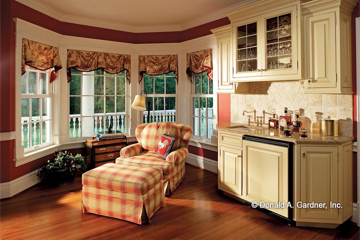 Interior view of a sitting area with a bay window, bar cabinetry, and plaid armchair.