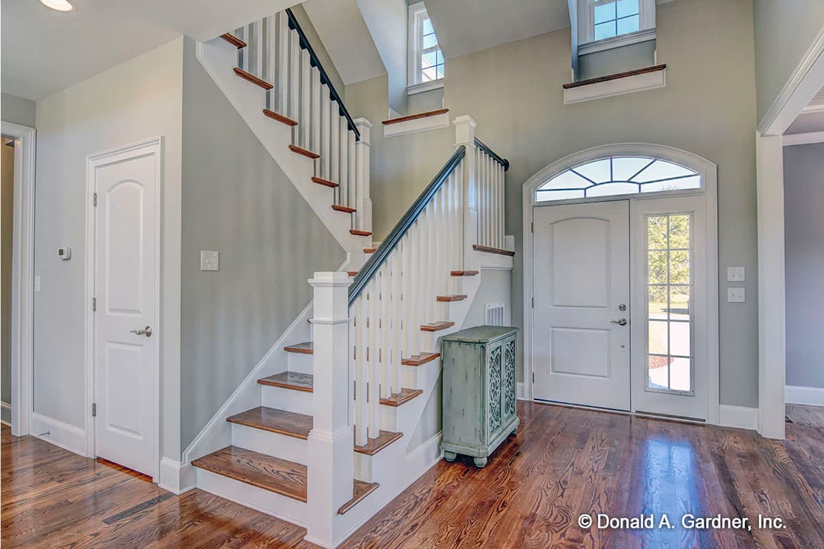 Interior view of a house entryway with a U-shaped staircase, double doors, and hardwood flooring.