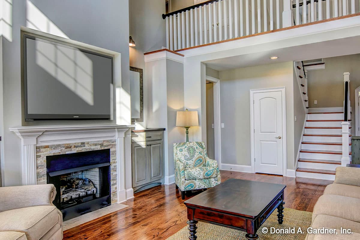 Great room with stone fireplace, built-in TV, open staircase to second floor loft, and wood flooring.