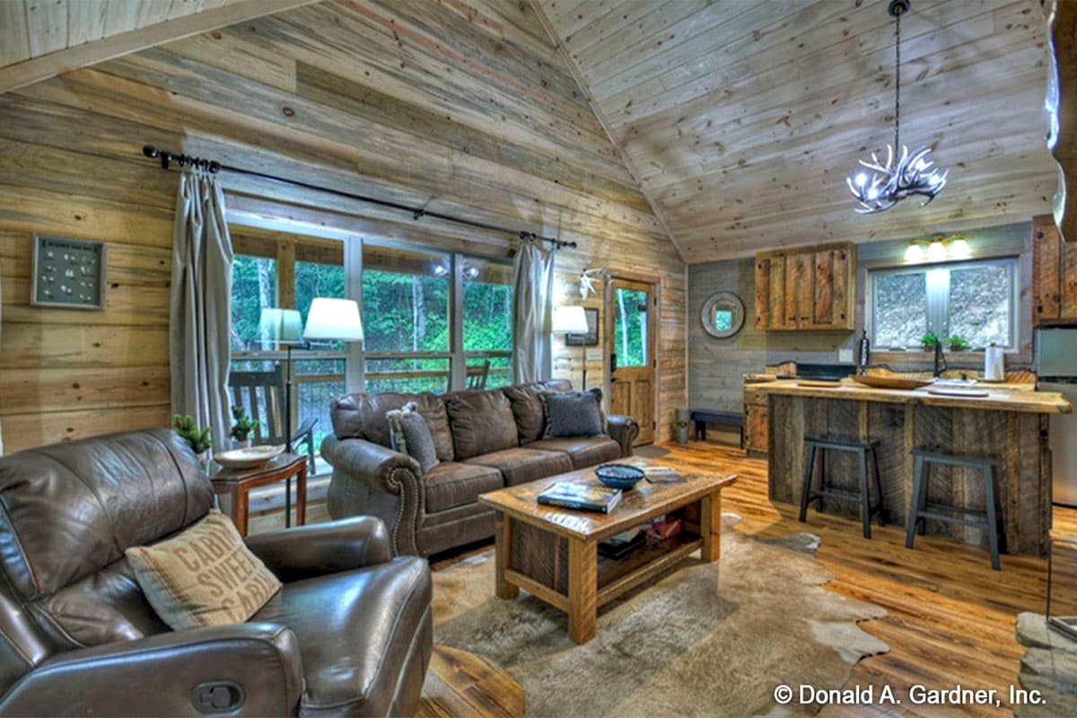Interior view of rustic living room with wood paneling, vaulted ceiling, leather seating, and kitchen island with bar stools.