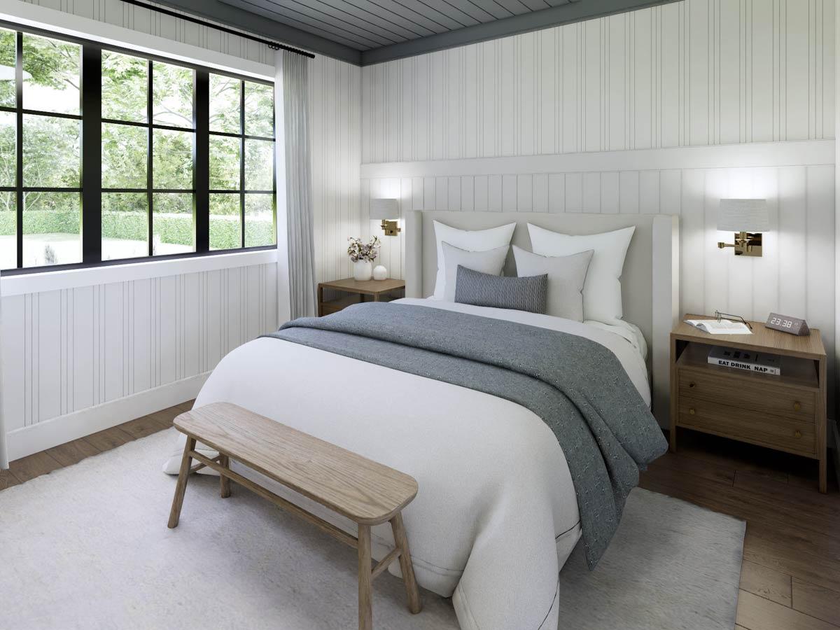 Cozy bedroom with a large window overlooking a lush garden. The room features a bed with white linens, a gray throw, and a wooden bench at the foot.