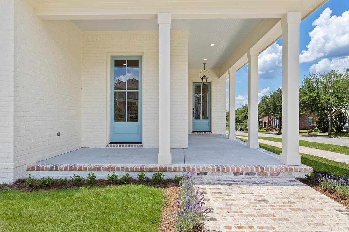 House plan exterior with white painted brick, a deep covered porch with white columns, and light blue paneled doors.