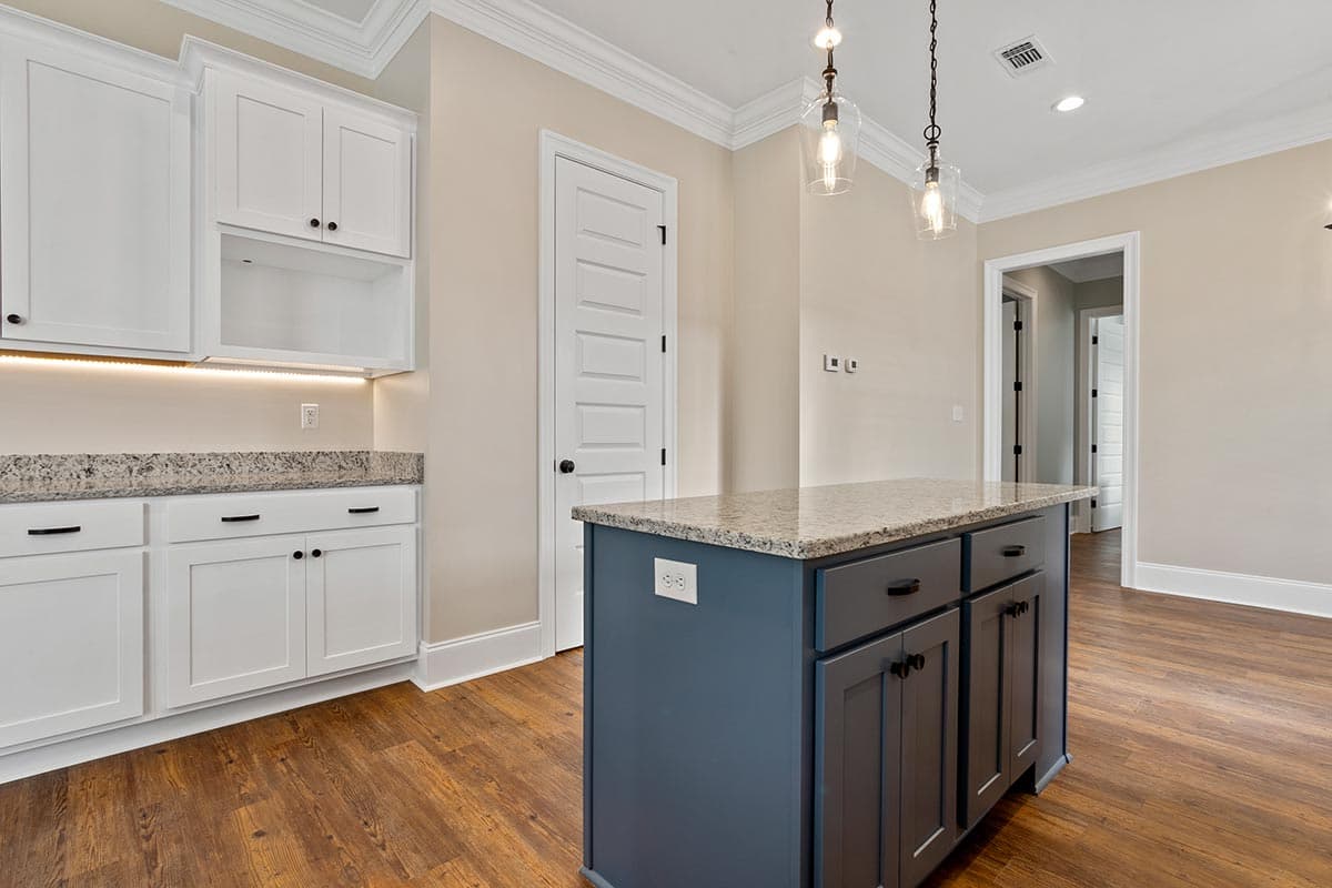 Kitchen with white shaker cabinets, granite countertops, island with dark blue base cabinets, and pendant lights.