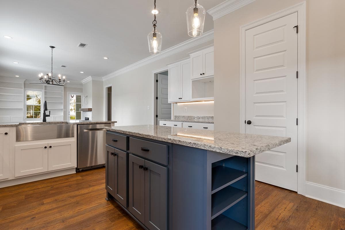 Kitchen with gray island, farmhouse sink, stainless steel dishwasher, white cabinets, granite countertops, and built-in shelving.