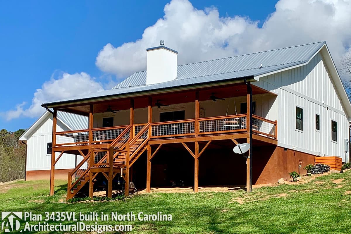 Modern Farmhouse plan exterior with white board and batten siding, a gabled roof, and a large wraparound deck with wooden stairs.