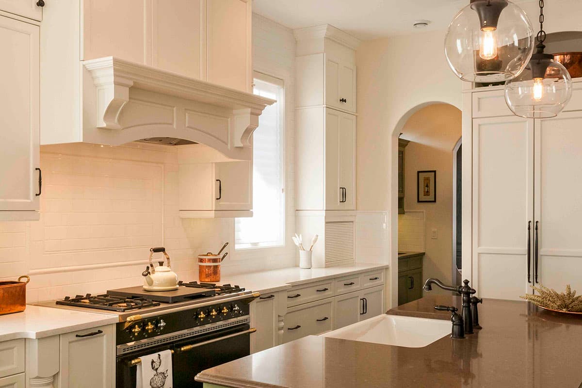 Interior kitchen view showing white cabinetry, a range hood with decorative molding, a gas range, and an arched doorway to another room.