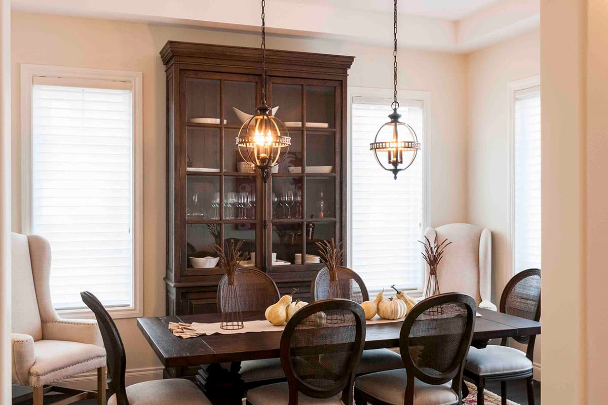 Dining room with dark wood table, cane-back chairs, china cabinet, and two globe pendant lights.