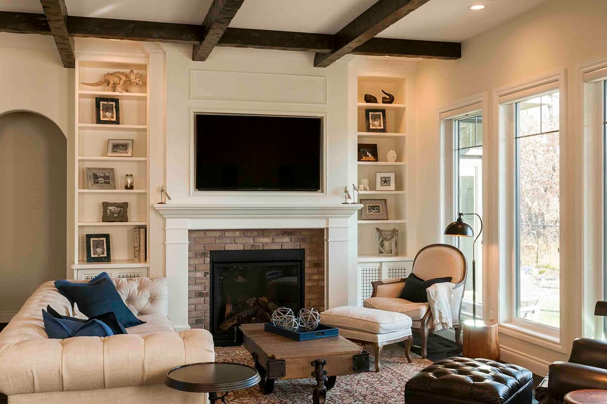 Living room with fireplace, built-in shelving, exposed beams, and large windows.