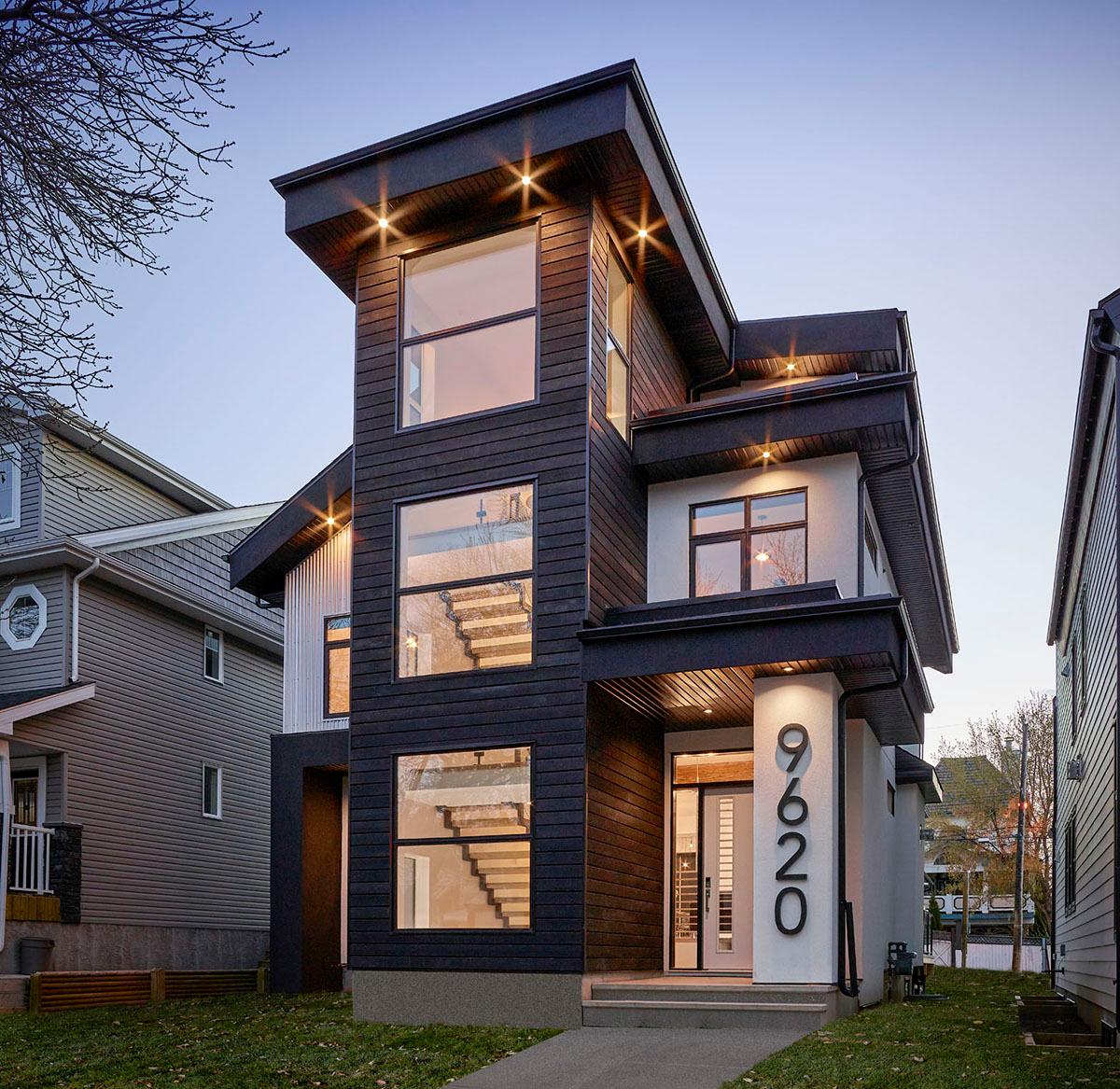 Modern house plan exterior. Two-story with flat rooflines, large windows, and dark siding. Features a covered entry and a concrete walkway.