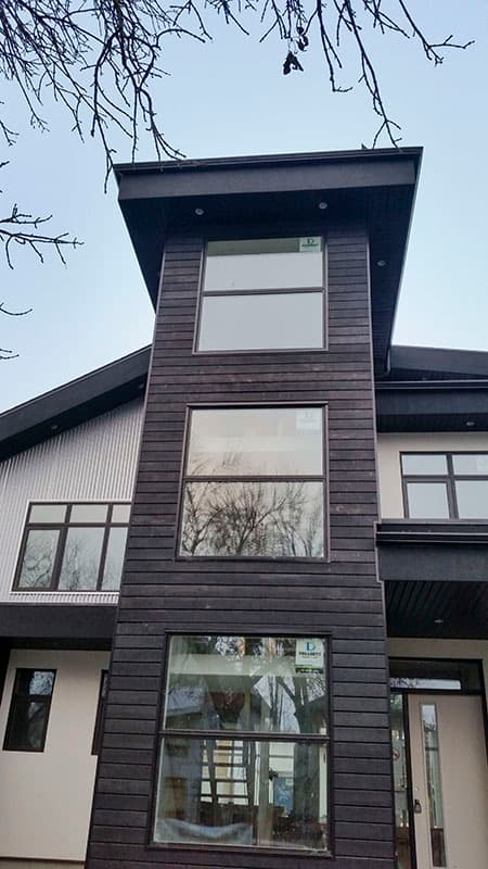 Modern house exterior with dark wood siding, a vertical tower with stacked windows, and corrugated metal accents.