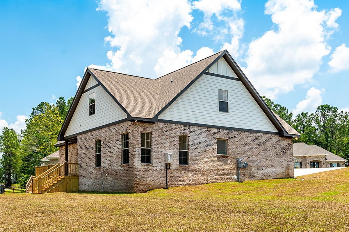 House plan exterior with brick facade, gable accents, and a prominent wooden staircase leading to the side entrance.