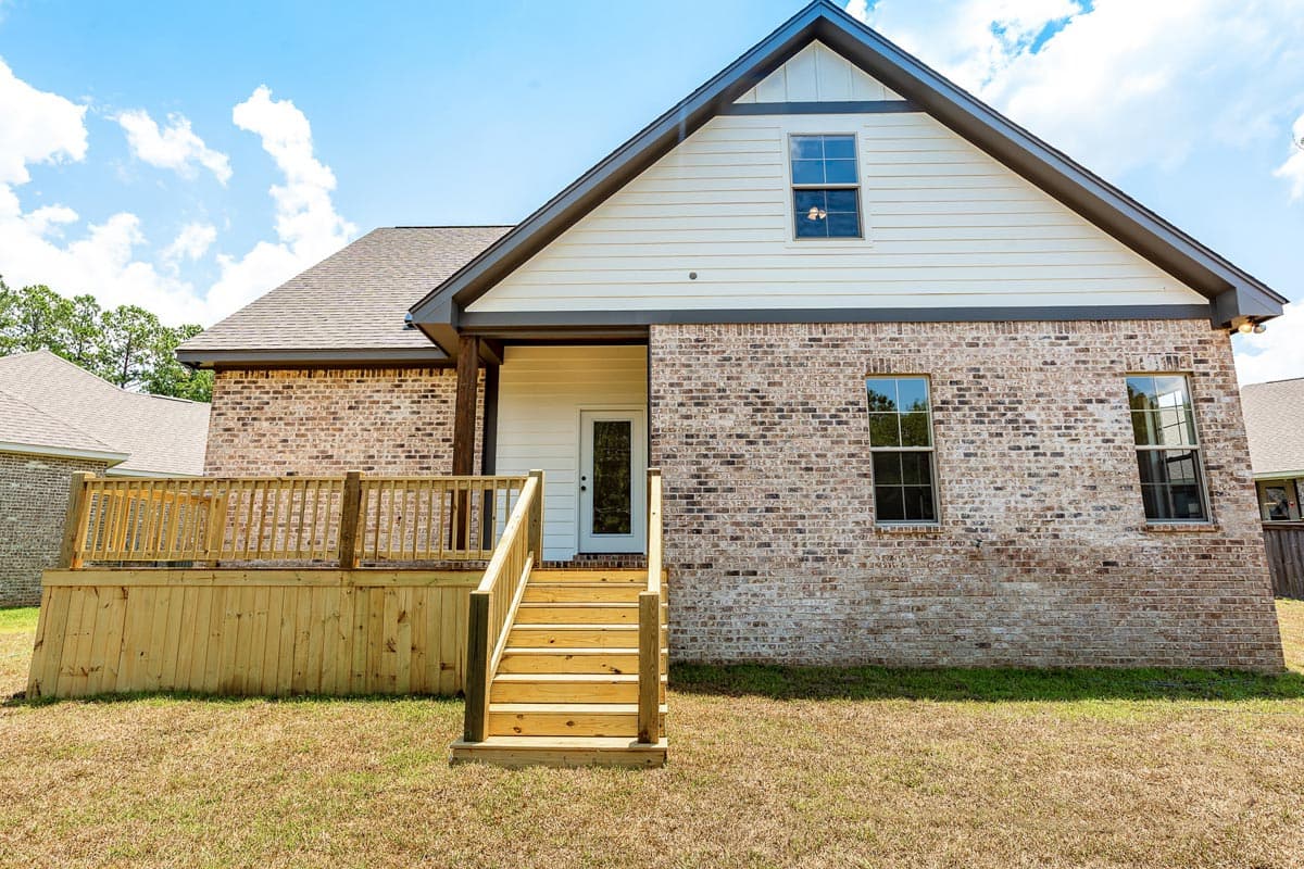 House plan exterior featuring brick facade, wood deck, covered entrance with door, and gabled dormer.