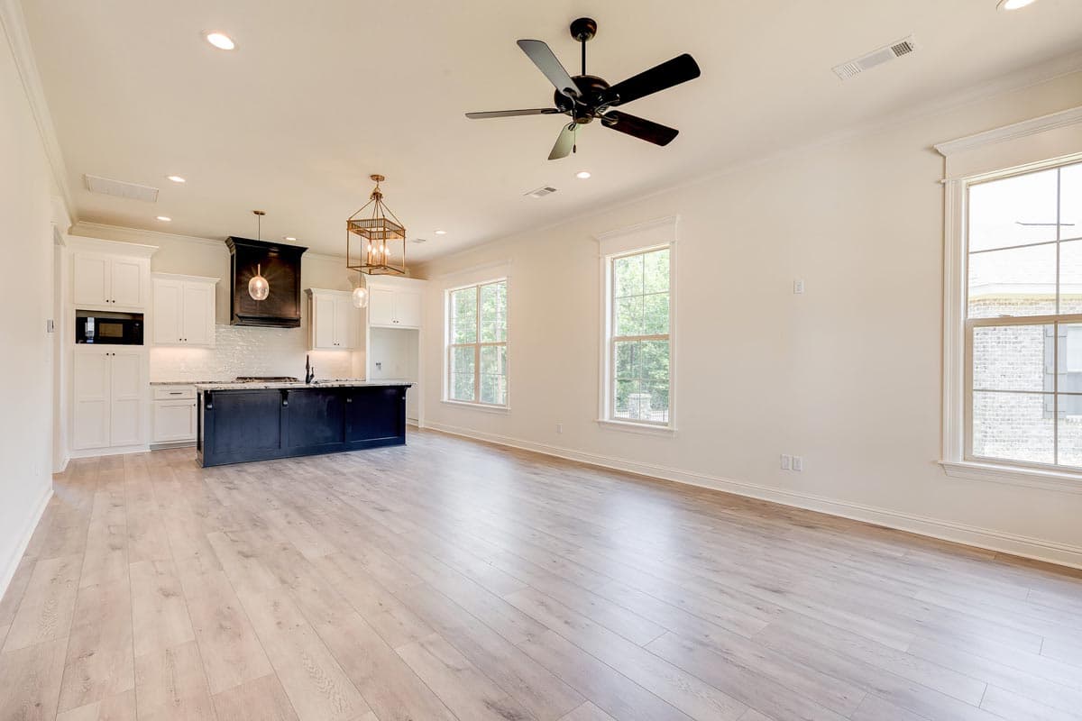 Open concept kitchen and living area with dark island, white cabinets, microwave, ceiling fan, and large windows.