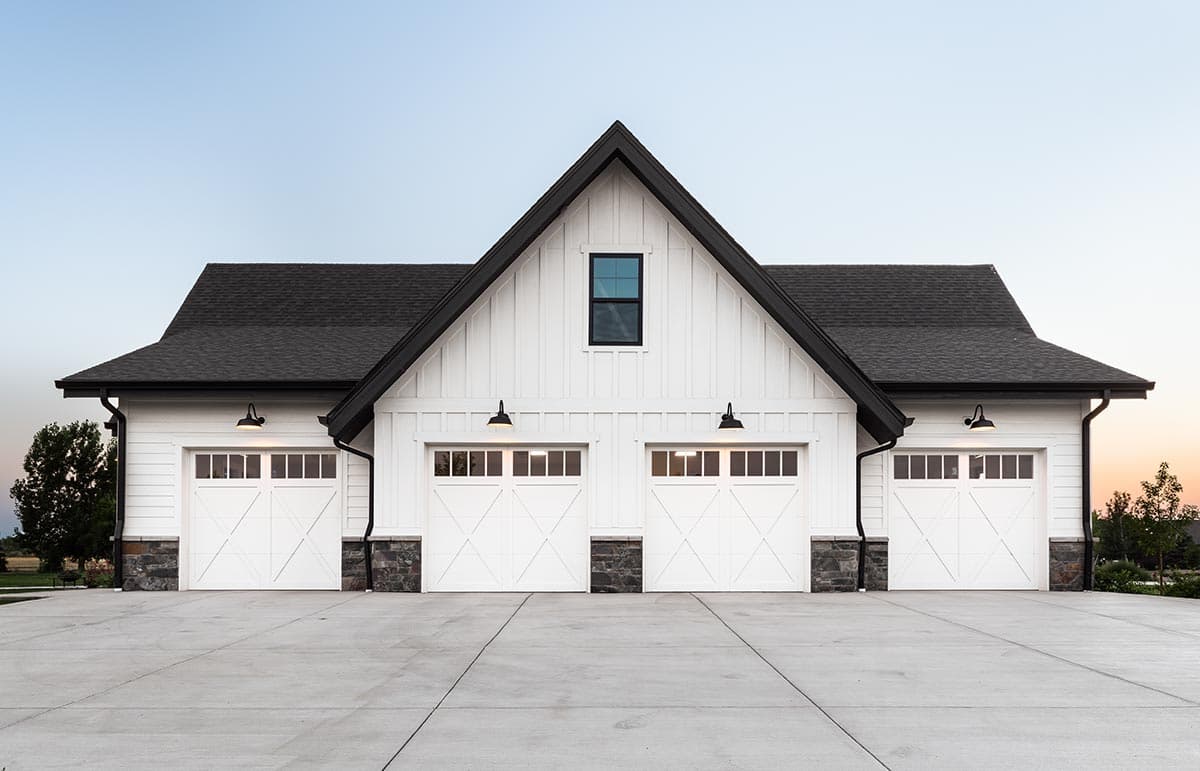Modern Farmhouse style house plan exterior with four garage doors, white board and batten siding, and stone accents.