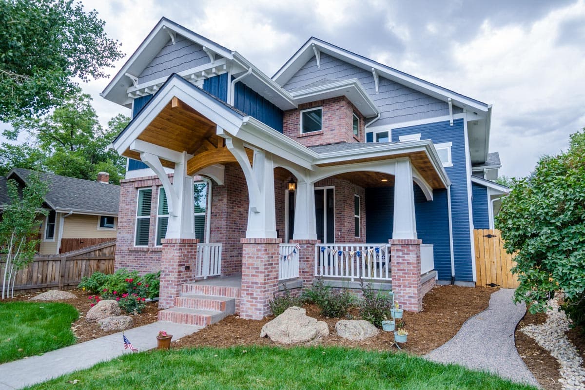 House plan exterior: Two-story Craftsman style with brick and blue siding, prominent gabled dormers, and a multi-columned wrap-around porch.