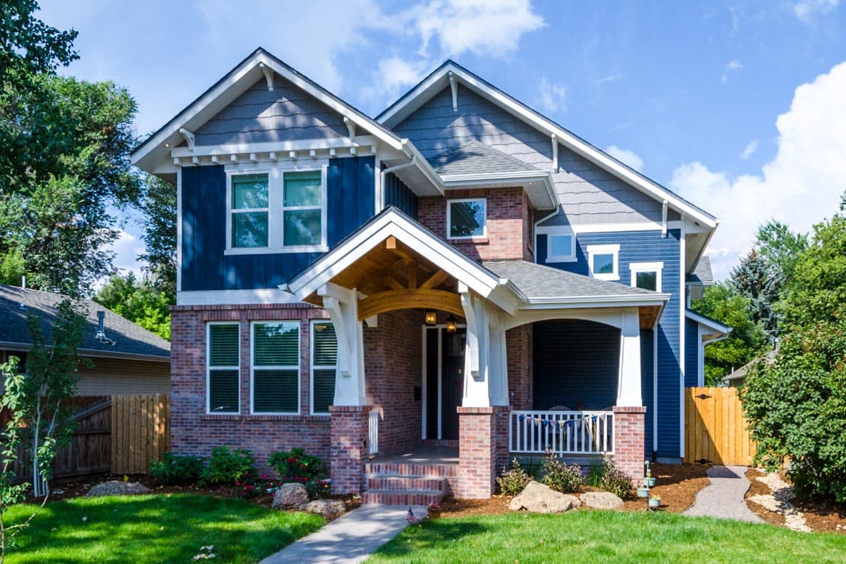 Craftsman style house plan exterior with brick and blue siding, prominent gabled dormers, and a covered entry porch with exposed wood beams.
