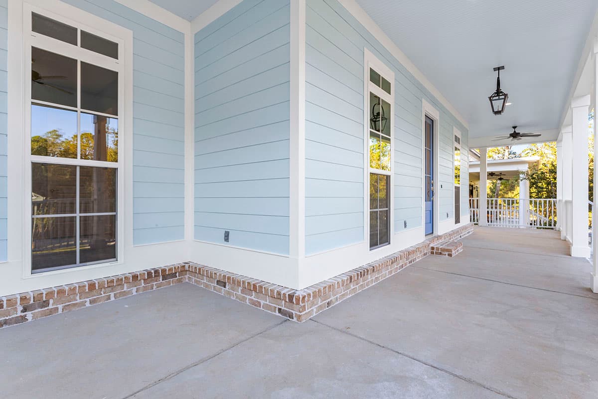 House plan exterior featuring light blue siding, brick foundation, large windows, a covered porch with white columns, and a light blue ceiling.