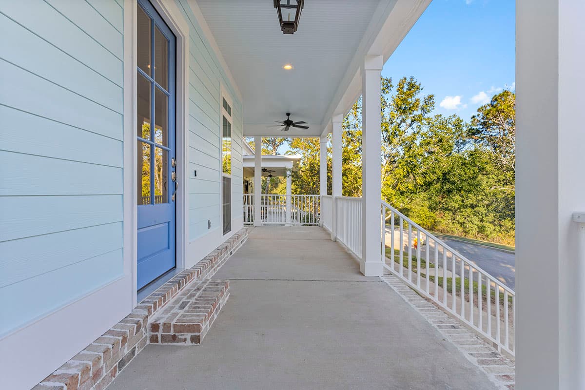 House plan exterior shows a light blue sided house with a wide wraparound porch, white railings, and a blue paneled door.