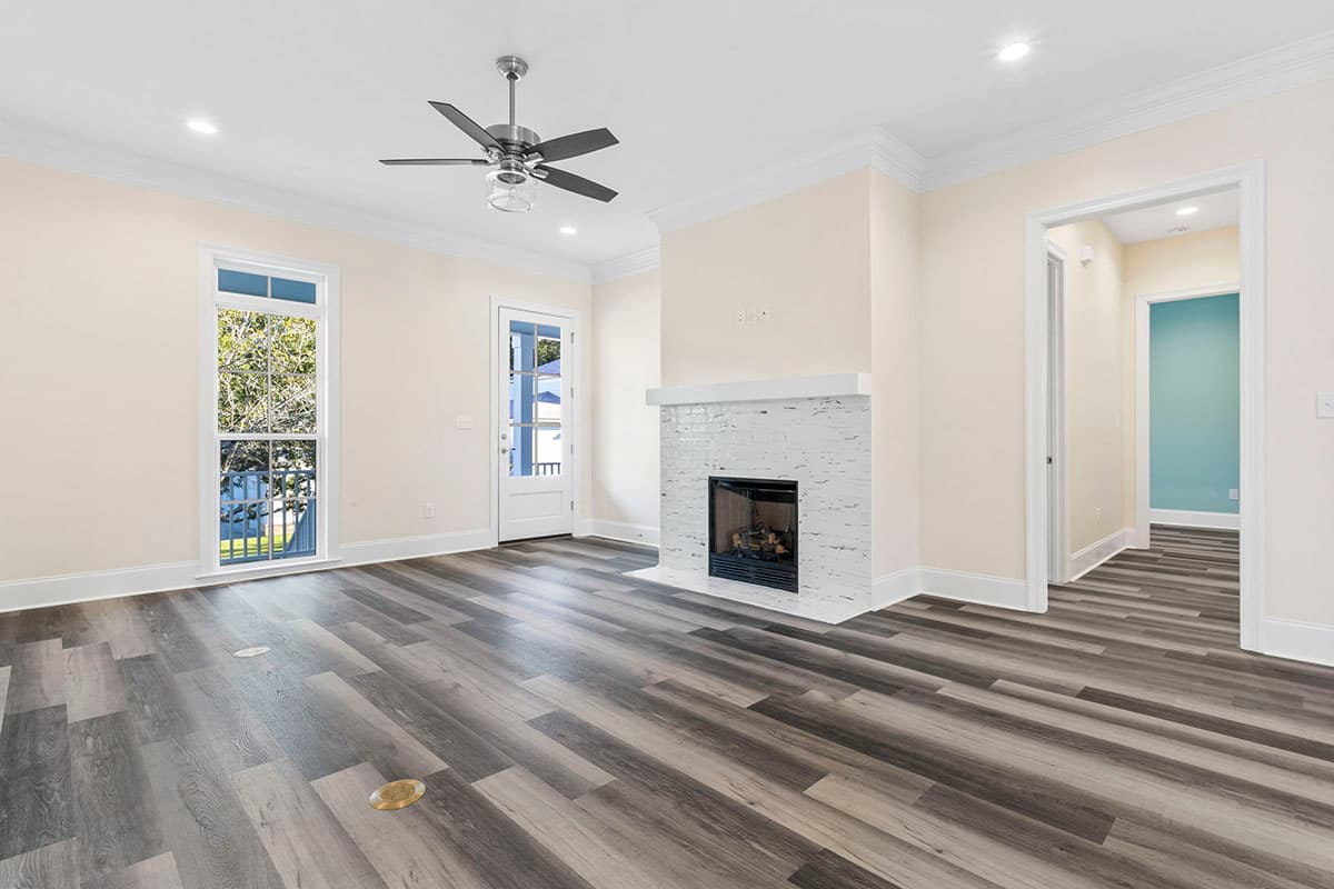 Interior view of a living room with a white brick fireplace, ceiling fan, and access to hallway.