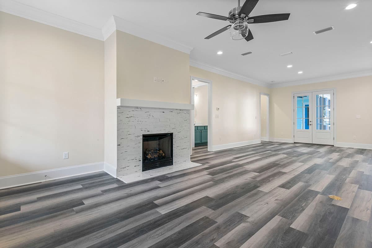 Interior rendering of a great room with a white brick fireplace, ceiling fan, and double doors leading outside.
