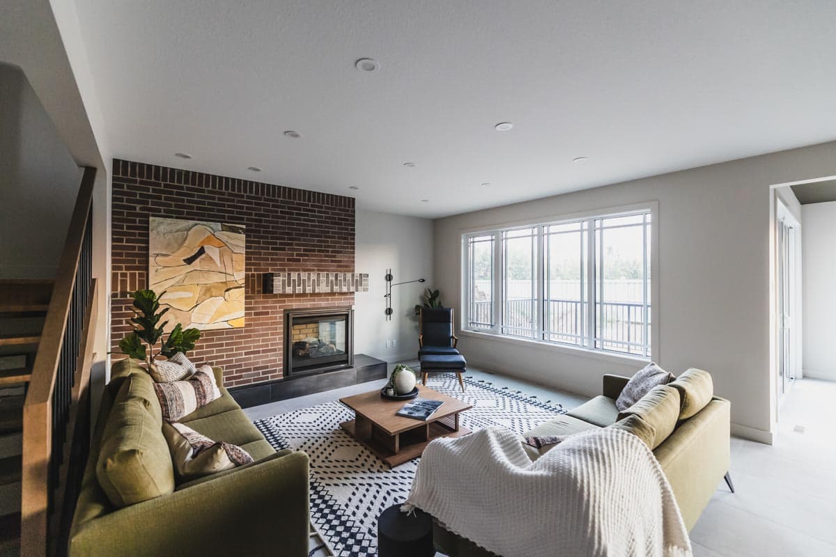 Living room interior with brick fireplace, large window, modern furniture, and patterned rug.