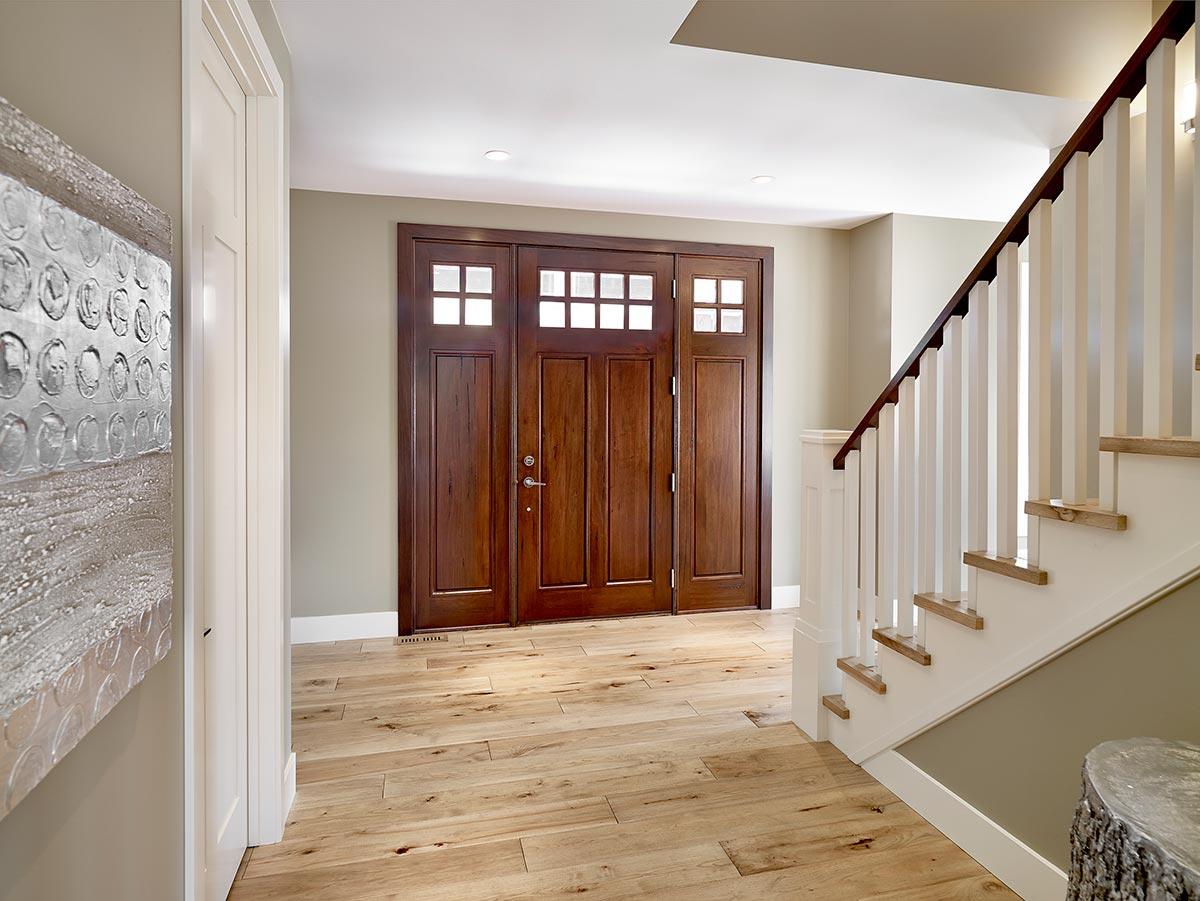 Interior view of a house entrance with double wooden doors with glass panes and a staircase with white banisters.