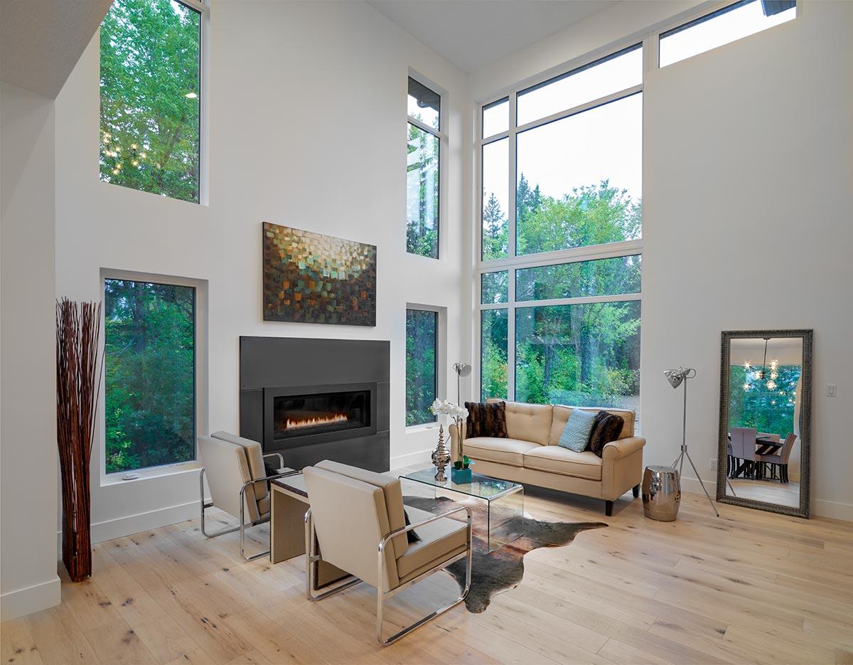 Modern living room with fireplace, sectional sofa, and floor-to-ceiling windows with forest view.