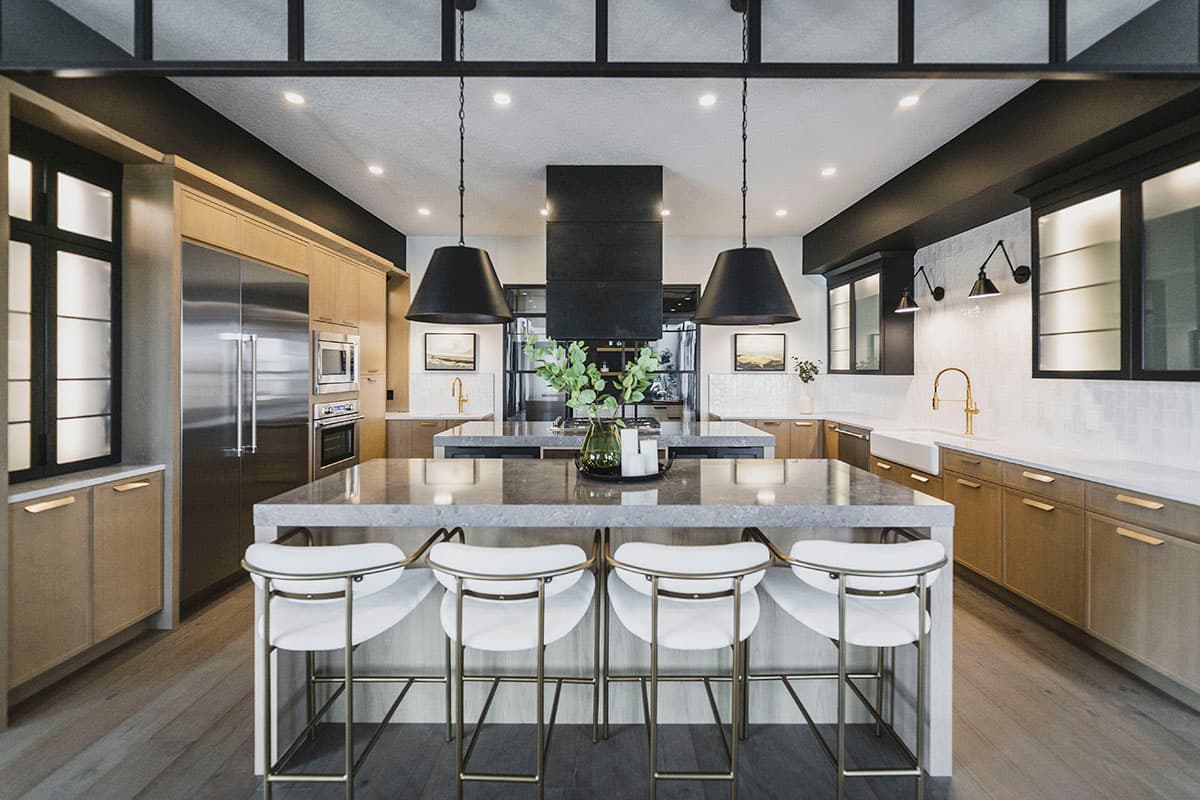 Modern kitchen with large island, stainless steel appliances, and two-tone cabinetry. Black pendant lights hang over the island.