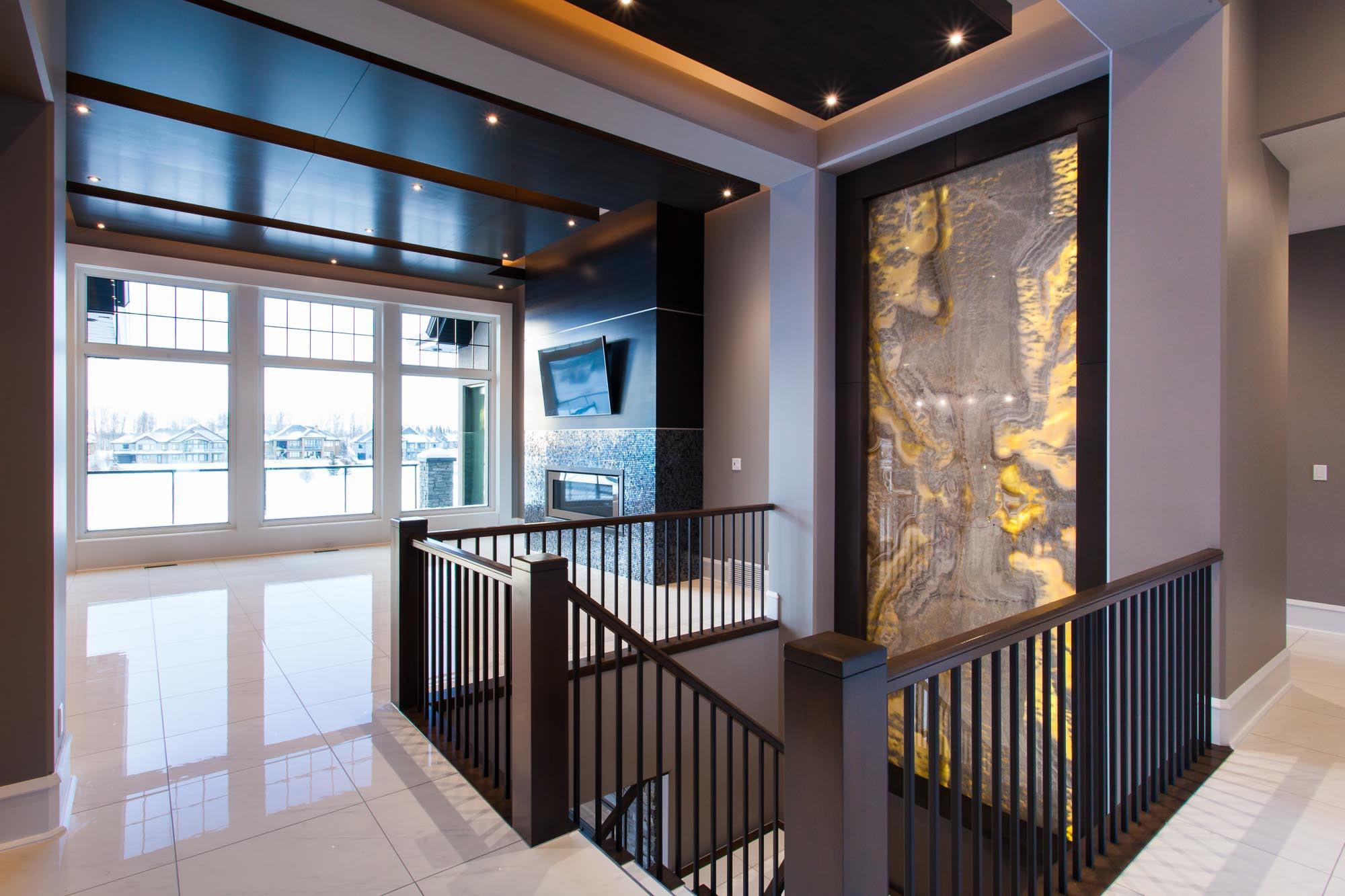 Interior view of a modern home with a grand staircase, fireplace, large windows, and decorative wall paneling.